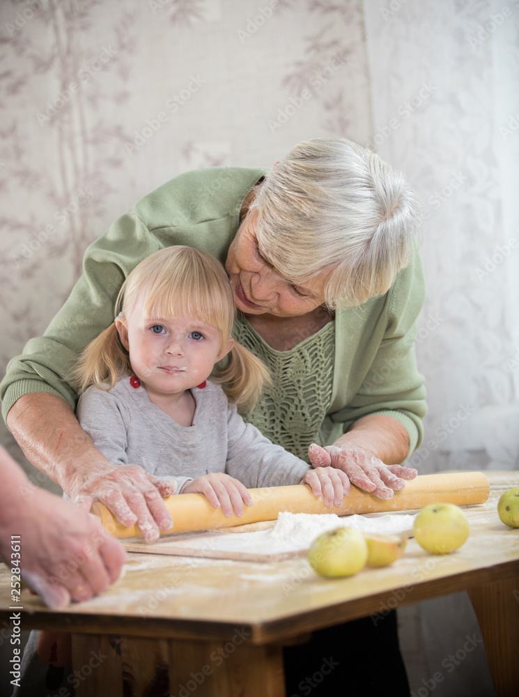 Obraz premium A grandmother making little pies with her granddaughter. Rolling the dough