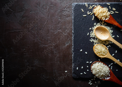 Rice of different varieties in wooden spoons on a dark background. Slate stone background. Plenty of room for text.