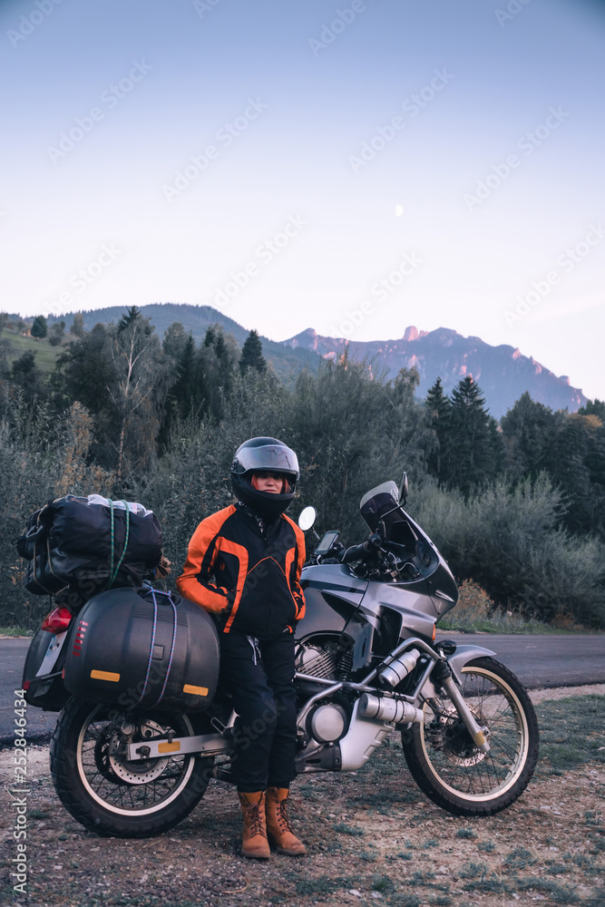 woman biker with adventure motorcycle parking on the side road, sunset, Ceahlau mountains and forest, Romania, tourism travel concept, motorcyclists way, vertical photo woman biker with adventure motorcycle parking on the side road, sunset, Ceahlau mountains and forest, Romania, tourism travel concept, motorcyclists way, vertical photo
