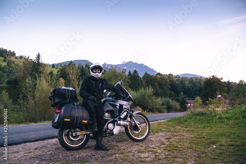 Rider Man and off tourism adventure motorcycles with side bags and equipment for long road trip, travel touring concept, Ceahlau, Romania, mountains on background, sunset evening