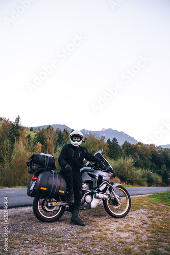 Rider Man and off tourism adventure motorcycles with side bags and equipment for long road trip, travel touring concept, Ceahlau, Romania, mountains on background, sunset evening, vertical photo