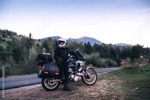 Fototapeta Naklejka Na Ścianę i Meble -  Rider Man and off tourism adventure motorcycles with side bags and equipment for long road trip, travel touring concept, Ceahlau, Romania, mountains on background, sunset evening