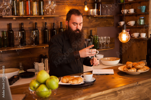 Beaded hipste waiter preparing cofffe behind the bar. photo