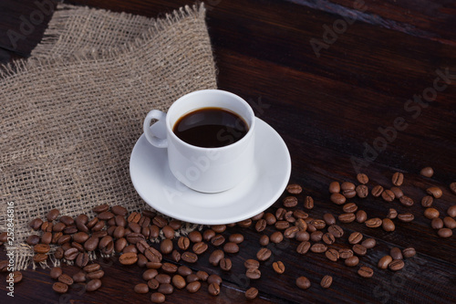 White cup of coffee with coffee grains near on linen fabric on the dark vintage background