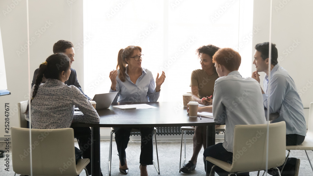 Middle-aged businesswoman speaking at diverse group negotiations at conference table