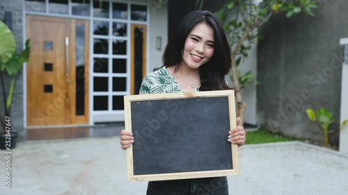 young asian woman holding blank black board in front of modern house photo