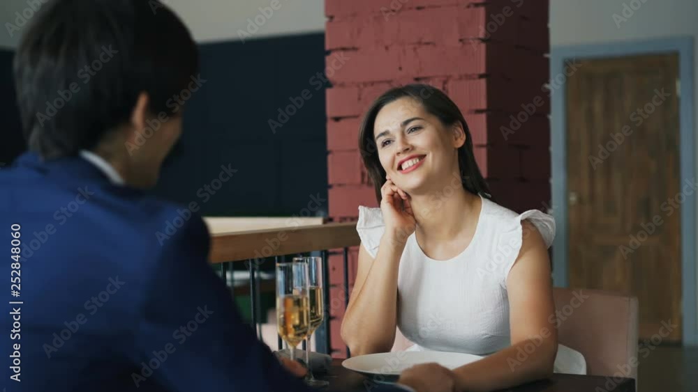 Happy young woman in beautiful dress is talking to her boyfriend on date sitting at table together holding hands. Romantic youth, dating and relationship concept. Happy young woman in beautiful dress is talking to her boyfriend on date sitting at table together holding hands. Romantic youth, dating and relationship concept.