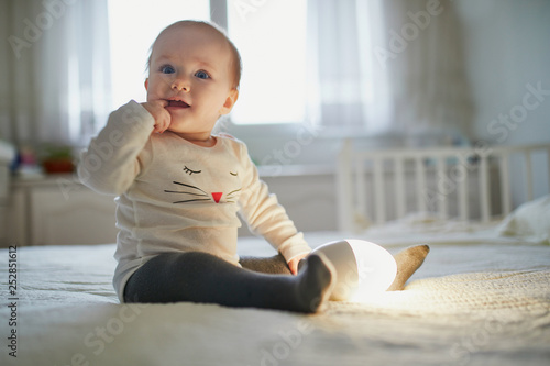 Billede på lærred Adorable baby girl playing with bedside lamp in nursery
