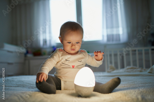 Photography Adorable baby girl playing with bedside lamp in nursery