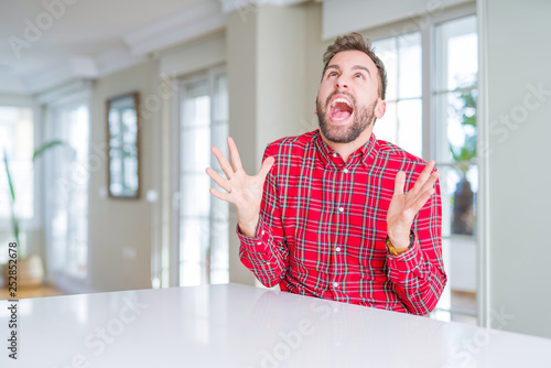 Handsome man wearing colorful shirt crazy and mad shouting and yelling with aggressive expression and arms raised. Frustration concept. © Krakenimages.com