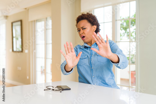 Young beautiful african american woman afraid and terrified with fear expression stop gesture with hands, shouting in shock. Panic concept.