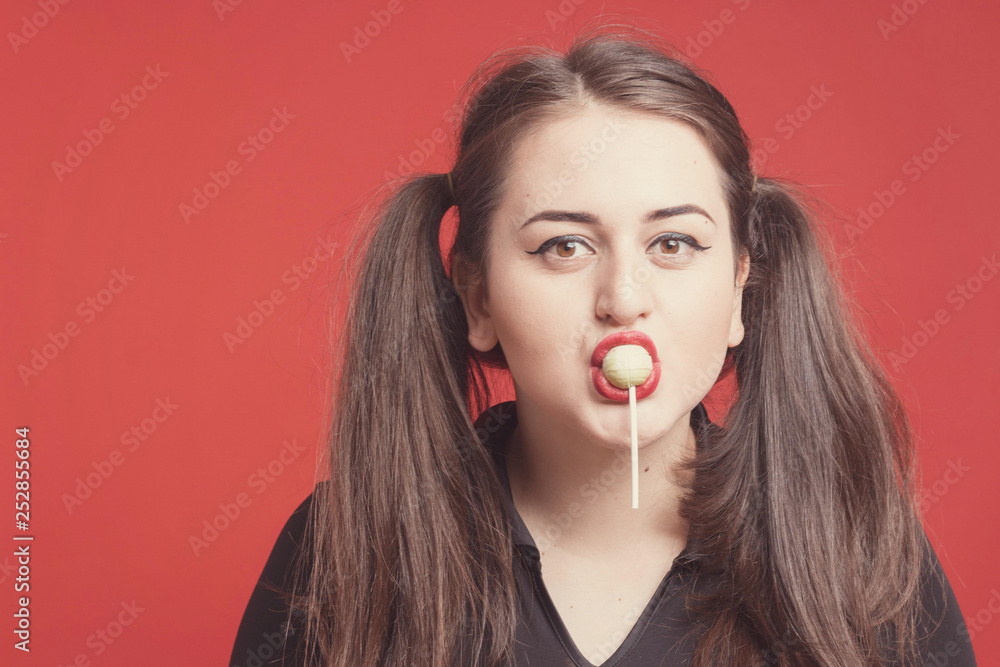 Model plus size with sweet donut, happy girl holding in hand candy and lick sweets, in black bodysuit. XXL female on red background Model plus size with sweet donut, happy girl holding in hand candy and lick sweets, in black bodysuit. XXL female on red background