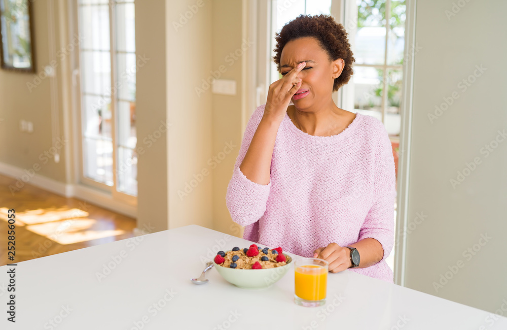 Young african american woman having healthy breakfast in the morning at home smelling something stinky and disgusting, intolerable smell, holding breath with fingers on nose. Bad smells concept. Young african american woman having healthy breakfast in the morning at home smelling something stinky and disgusting, intolerable smell, holding breath with fingers on nose. Bad smells concept.