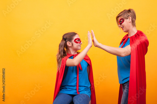 Mother and daughter dressed like superheros giving hi5 over yellow background.