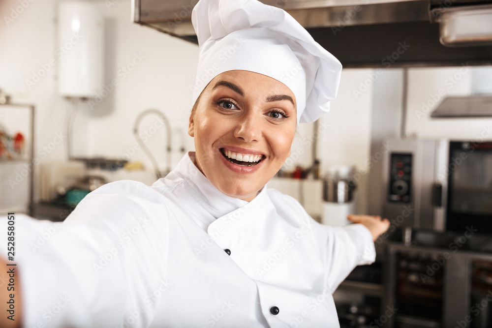 Portrait of pretty woman chef wearing white uniform, taking selfie photo in kitchen at the restaurant