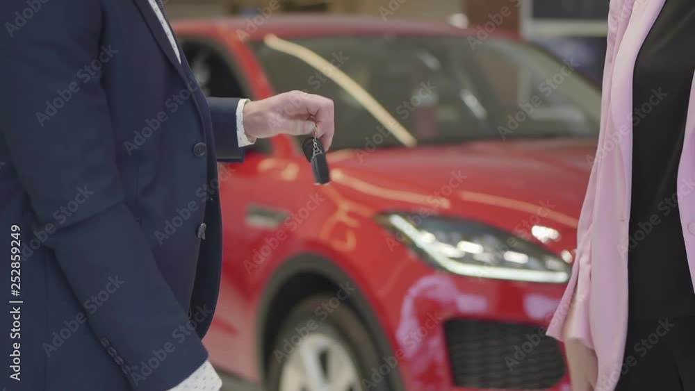 Unrecognized seller sends the keys to the new auto to the new owner. A man in a business suit entered into an agreement to buy a new vehicle. Car showroom. Unrecognized seller sends the keys to the new auto to the new owner. A man in a business suit entered into an agreement to buy a new vehicle. Car showroom.