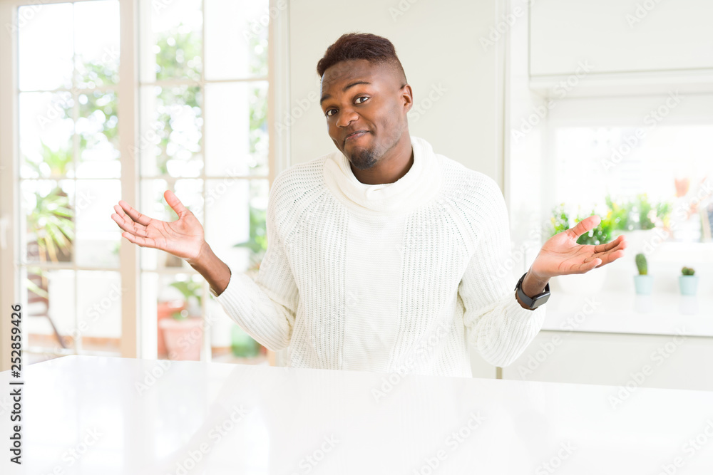 Handsome african american man on white table clueless and confused expression with arms and hands raised. Doubt concept. Handsome african american man on white table clueless and confused expression with arms and hands raised. Doubt concept.