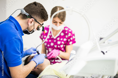 Male dentist and female assistant checking up patient teeth with dental tools microscope  mirror and probe at dental clinic office. Medicine  dentistry and health care concept. Dental equipment