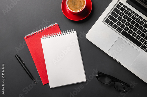 Blank notepad over laptop and coffee cup on office black table.