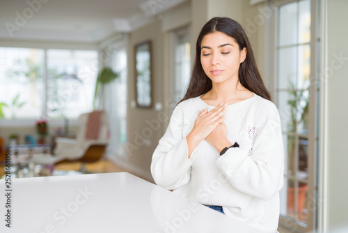 Free Download Young beautiful woman at home on white table smiling with hands on chest with closed eyes and grateful gesture on face. Health concept. - GFXLoad