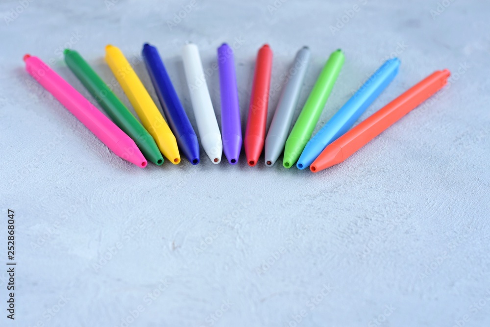 Row of colorful pen with selective focus on gray textured background. Back to school flat lay. Beautiful rainbow pens on grey cement backdrop. Multicolored education tools for drawing