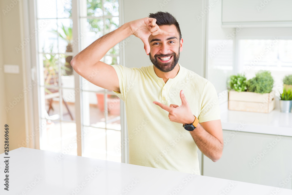 Handsome hispanic man casual yellow t-shirt at home smiling making frame with hands and fingers with happy face. Creativity and photography concept. Handsome hispanic man casual yellow t-shirt at home smiling making frame with hands and fingers with happy face. Creativity and photography concept.