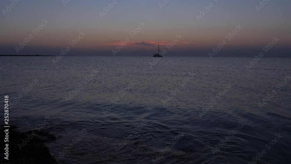 sunset over the calm surface of the sea, a lonely yacht and the movement of the setting sun through the clouds over the sea horizon sunset over the calm surface of the sea, a lonely yacht and the movement of the setting sun through the clouds over the sea horizon