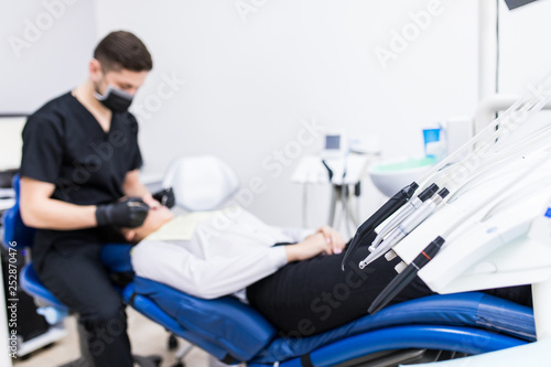 Great mood. Beautiful young woman sitting in the dentist chair and laughing together with her dentist while checking her teeth. Focus on equipment.
