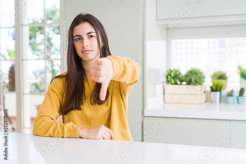 Beautiful young woman wearing yellow sweater looking unhappy and angry showing rejection and negative with thumbs down gesture. Bad expression.