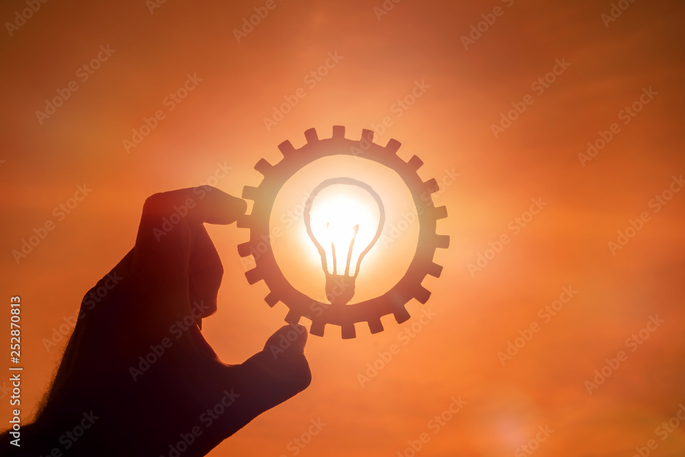 Gear light bulb in the hand of a man against the evening sky. the concept of the business idea