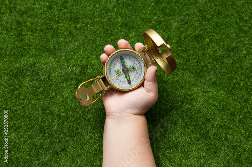 tourist compass in the hand of a man on the background of artificial green grass. tourism, sports, recreation.