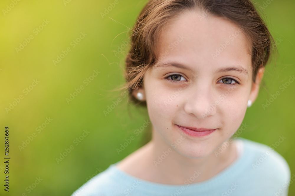 closeup portrait of happy smiling little caucasian girl in earrings and blue blouse on warm green background closeup portrait of happy smiling little caucasian girl in earrings and blue blouse on warm green background