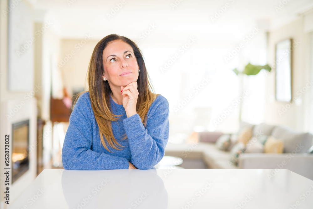 Beautiful middle age woman at home with hand on chin thinking about question, pensive expression. Smiling with thoughtful face. Doubt concept. Beautiful middle age woman at home with hand on chin thinking about question, pensive expression. Smiling with thoughtful face. Doubt concept.