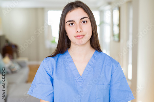 Beautiful young nurse woman at the clinic with serious expression on face. Simple and natural looking at the camera.