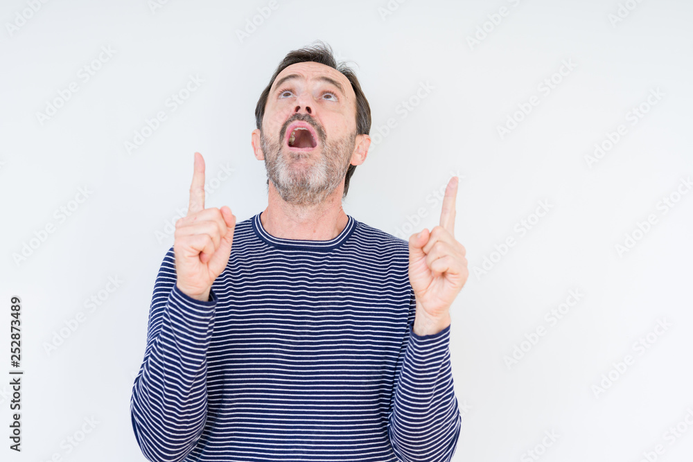 Handsome senior man over isolated background amazed and surprised looking up and pointing with fingers and raised arms. Handsome senior man over isolated background amazed and surprised looking up and pointing with fingers and raised arms.