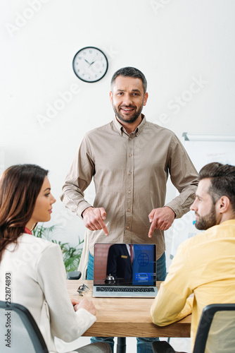 advisor pointing with fingers at laptop with booking website on screen to investors in office