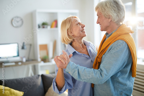 Side view portrait of loving senior couple dancing at home, copy space