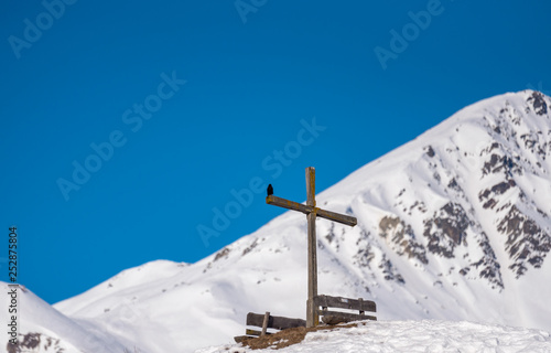 a cross between two benches at the top of a hill in winter.