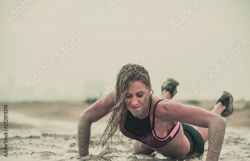 Closeup of strong athletic woman crawling in wet muddy puddle with mud on her face in an extreme competitive sport photo
