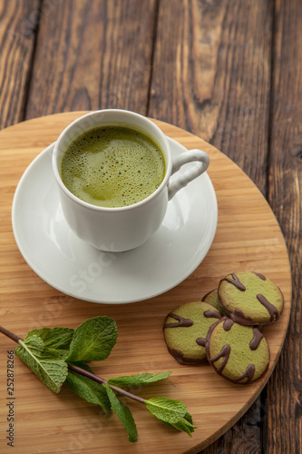 cup of Matcha tea and green cookies on a round wooden tray