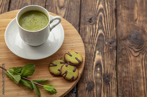 cup of Matcha tea and green cookies on a round wooden tray