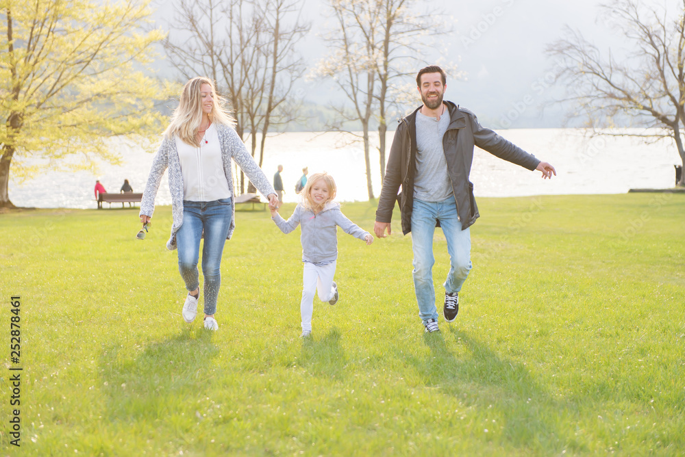 Happy father, mother and little girl running alongside lake and enjoying on a beautiful sunny day. Happy father, mother and little girl running alongside lake and enjoying on a beautiful sunny day.