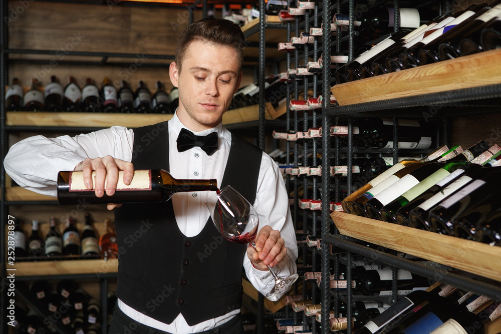 Let me introduce to you. Shot of a handsome professional sommelier pouring some wine into the glass for wine tasting