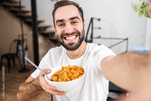 Happy man taking a selfie while sitting at the kitchen