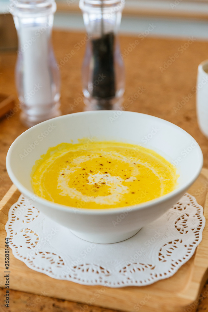 Classic Pureed Pumpkin Soup topping with Milk, Cream and Pepper. Served on wooden plate with salt, garlic and cutlery. Classic Pureed Pumpkin Soup topping with Milk, Cream and Pepper. Served on wooden plate with salt, garlic and cutlery.