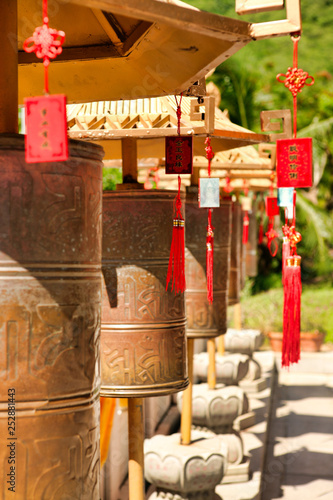 Buddhist prayer wheels in front of the temple jade-gold statue of the goddes Guanyin in the Nanshan park. On prayer wheels Mantra words are written. Hainan, Sanya.