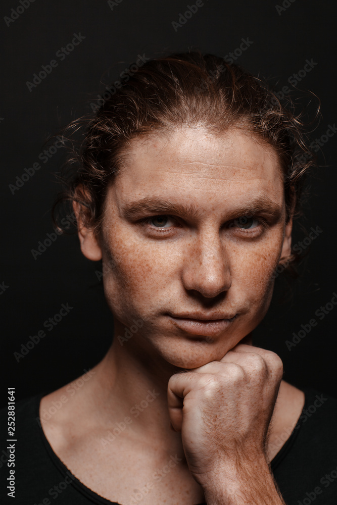 Portrait of a handsome long-haired man with drawn hair and freckles wearing a black T-shirt