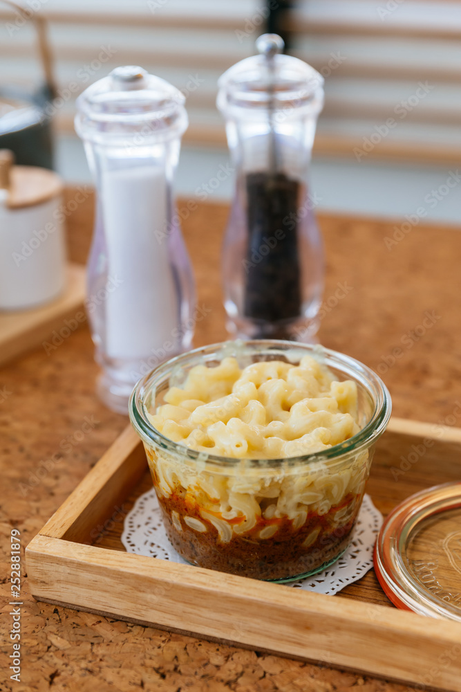 Macaroni Cheese Baked with meat sauce in glass bowl on wooden plate with salt, pepper and cutlery. Macaroni Cheese Baked with meat sauce in glass bowl on wooden plate with salt, pepper and cutlery.