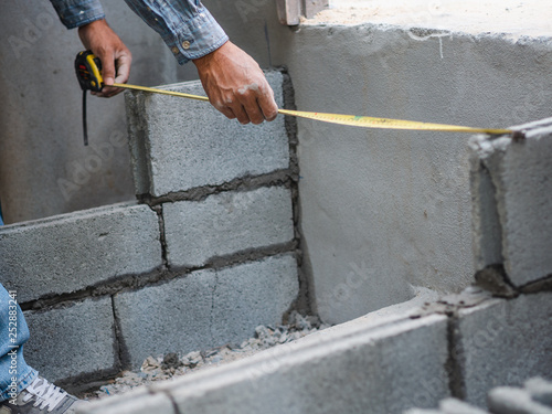 professional construction worker uses measuring Tape for measure and laying bricks with cement.