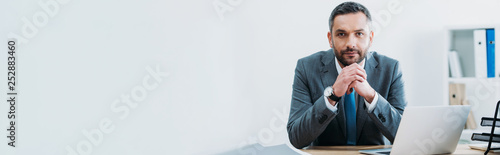 businessman sitting at table with laptop and looking at camera in office photo